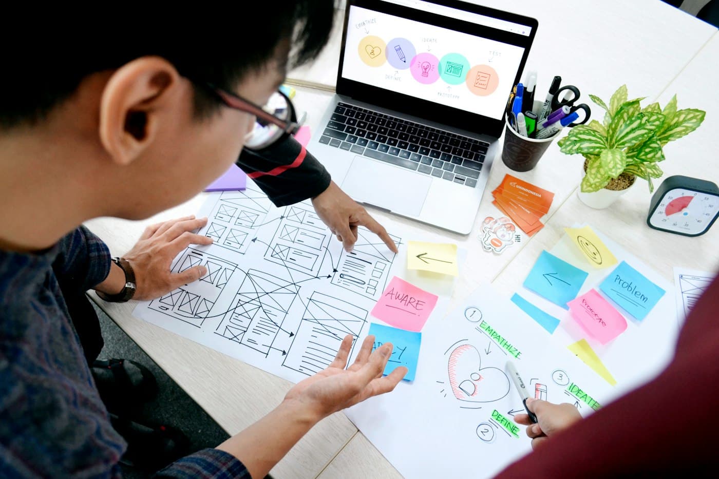 Designer sketching app screens on paper next to a laptop
