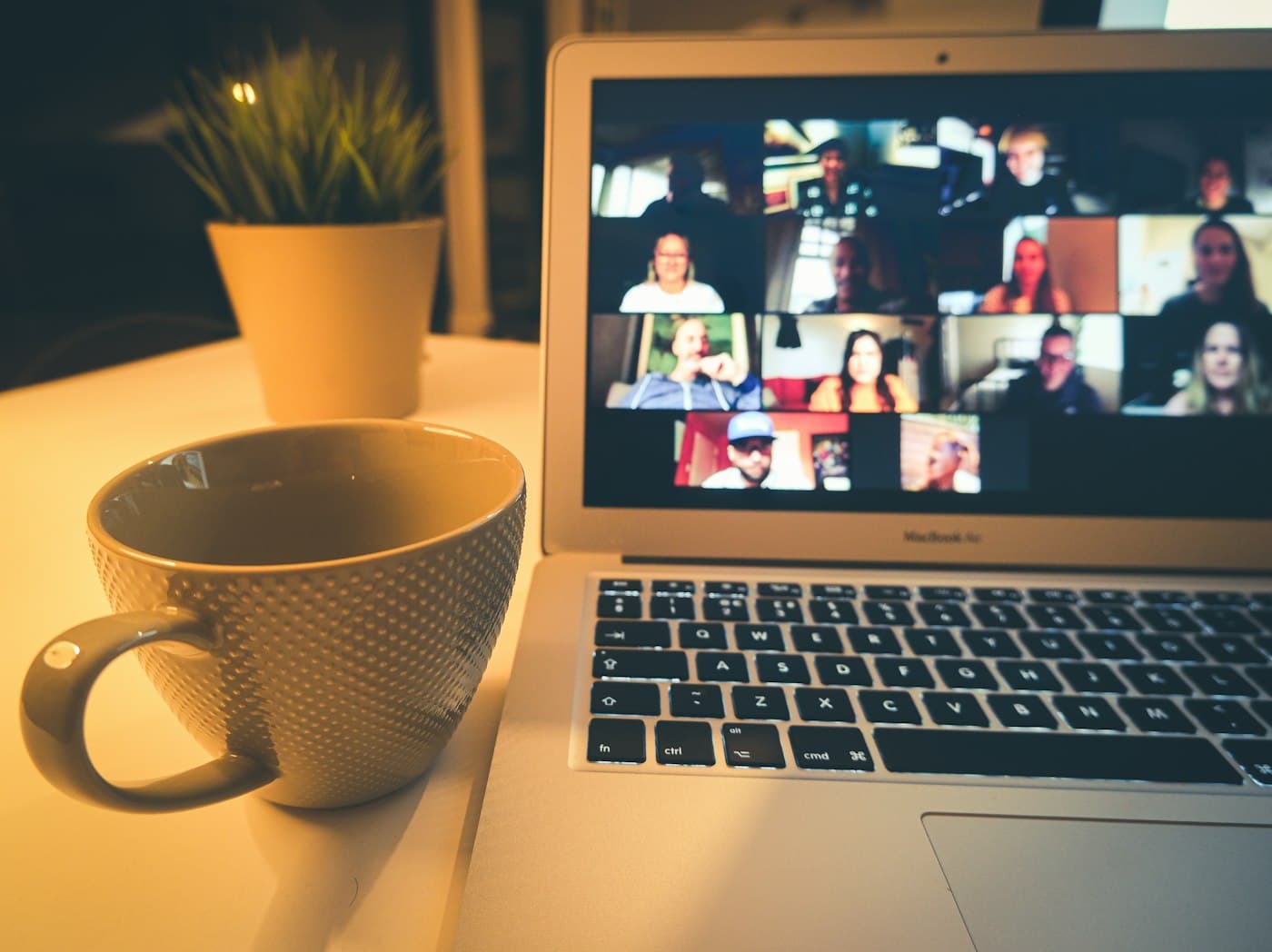Laptop on a desk showing a video call, next to a cup of coffee