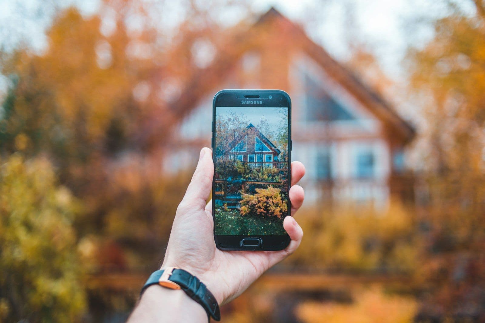 Hand holding a phone that shows a photo of the house behind it