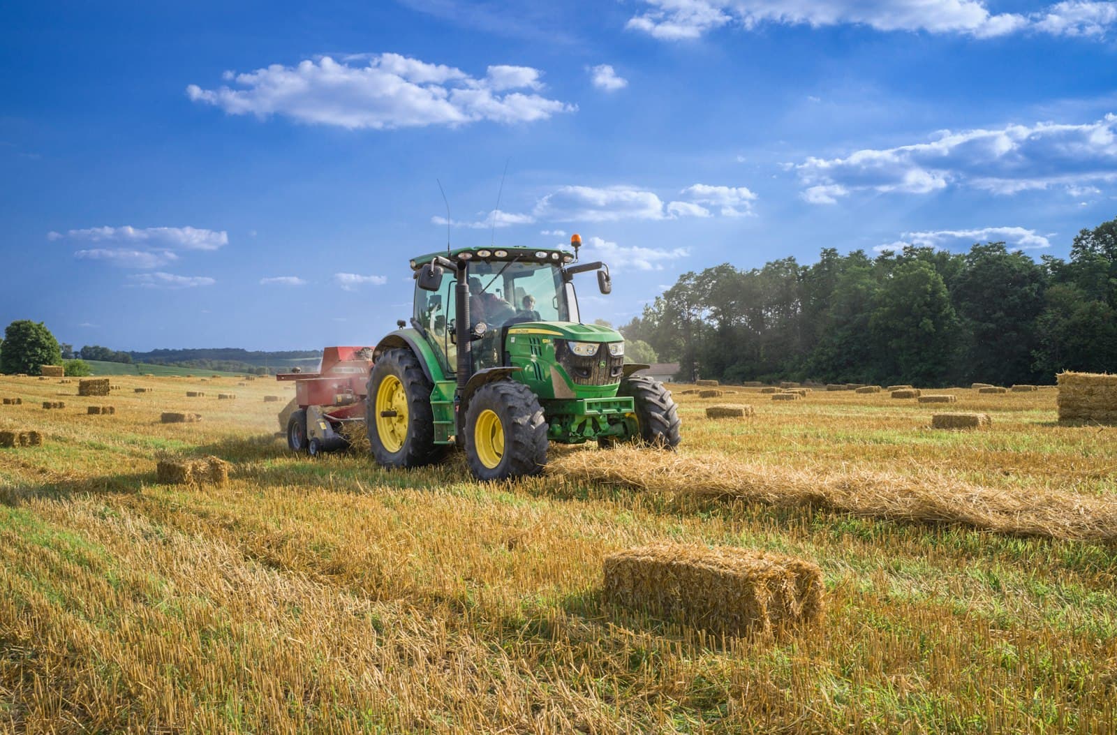 Green tractor baling hay in a harvested field